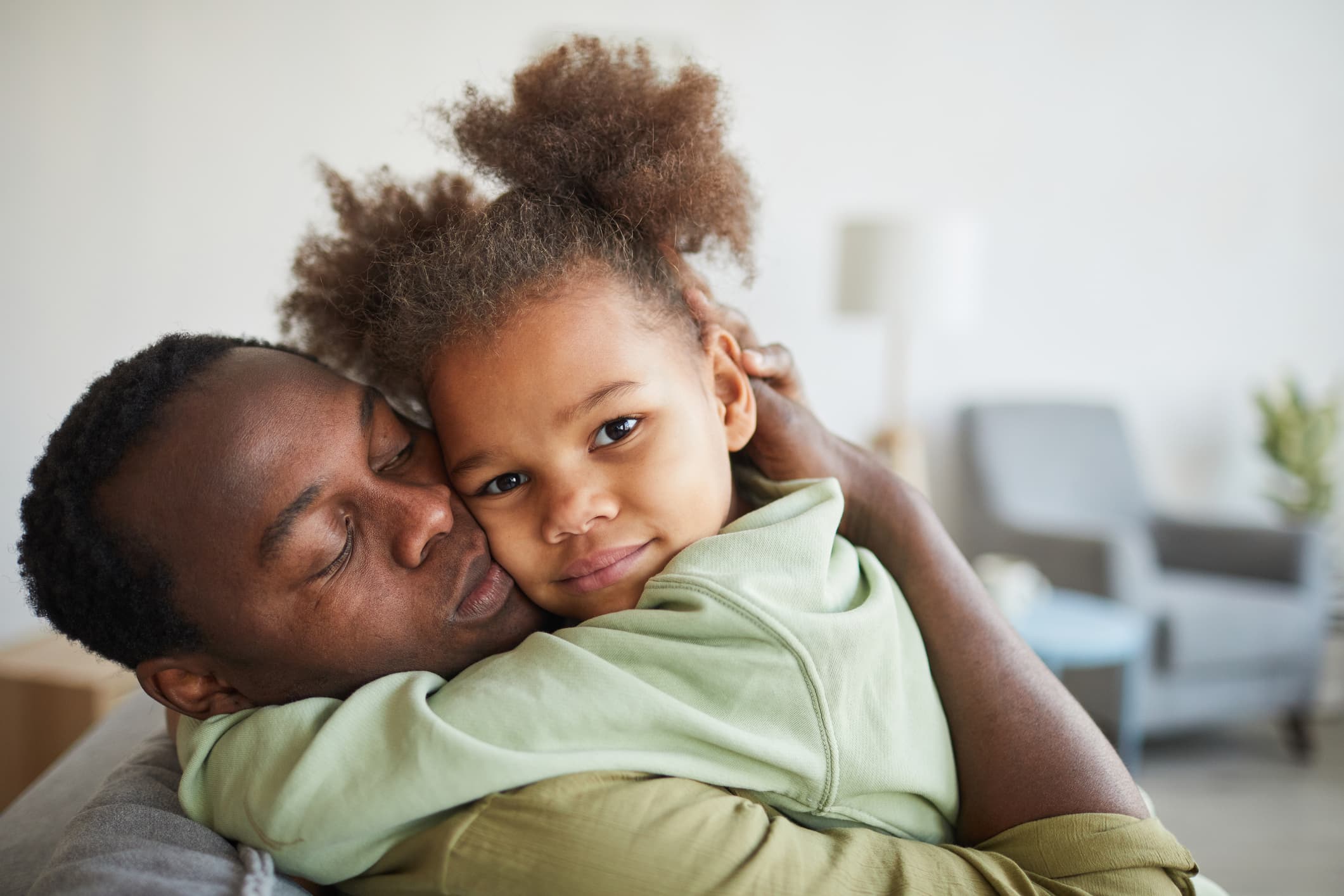 Portrait of cute African-American girl embracing father and looking at camera in cozy home interior, copy space